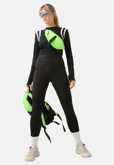 Black long-sleeve top with white stripes, black high-waisted leggings, green waist bag, and cream sneakers with texture details.