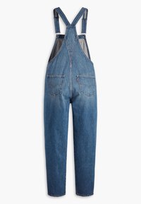 Vue arrière d'une salopette en denim bleu avec bretelles ajustables et deux poches arrière sur fond blanc.