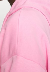 Felpa con cappuccio rosa chiaro caratterizzata da una trama morbida, una tasca a marsupio e dettagli di cucitura discreti lungo le cuciture.