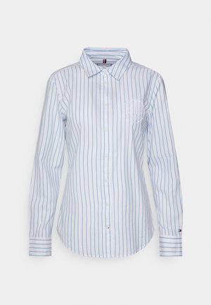 Chemise blanche à manches longues avec des rayures verticales bleu clair, un col, et un petit logo brodé sur la poitrine gauche et le poignet.