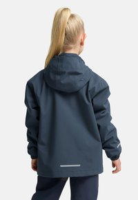 Giacca impermeabile navale con cappuccio, polsini elasticizzati e dettagli riflettenti. Presenta una vestibilità rilassata e un orlo curvo per una maggiore copertura.
