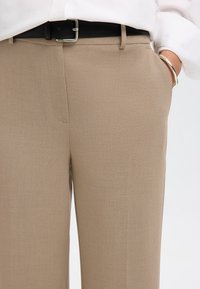 Pantaloni eleganti beige con una texture liscia, vestibilità su misura, tasche laterali e una cintura in pelle nera con fibbia argentata.
