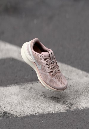 Lichtroze sportshoe met een bovenkant van mesh, een ronde vorm, grijze accenten en een witte zool, getoond zwevend boven een grijze achtergrond.