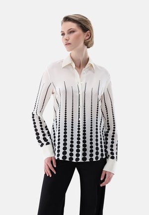 Weißes Blusenshirt mit schwarzen Punkten, ausgestattet mit einem Kragen, durchgehender Knopfleiste und langen Ärmeln. Glatte Stoffoberfläche mit einem Farbverlaufsdesign.