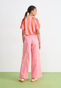 Camisa corta de mangas en rayas coloridas de rosa y naranja, combinada con pantalones rosas holgados. Ambos presentan una tela ligera y suave.