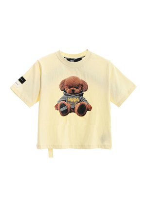 Camiseta de manga corta de color amarillo claro con un oso de peluche marrón con una sudadera con capucha gris estampada en la parte delantera y un parche en blanco y negro en la manga.