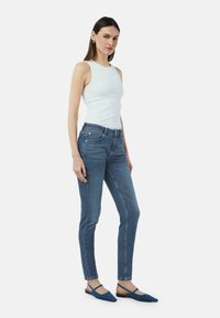 Lichtblauwe skinny jeans met een hoge taille, voorzien van vijf zakken en subtiele stiksels. Gecombineerd met een witte geribbelde tanktop en blauwe flats.
