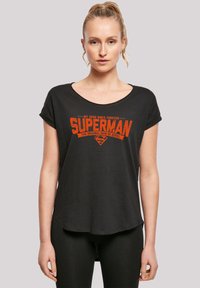 Sort kortærmet t-shirt lavet af blødt stof, der har et orange grafisk tryk med teksten "MIT HELD Siden FOR EVIGT SUPERMAN" og logo.