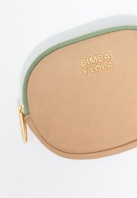 Beež riidekott, millel on roheline punutud tõmblukk. Sisaldab reljeefset brändinime "BIMBA Y LOLA" kullaga. Sile tekstuur, ümar kuju.