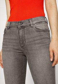 Jeans de mezclilla gris con una cintura de altura media, que cuentan con cinco bolsillos y detalles de costura sutiles. La tela tiene una textura suave y un ligero estiramiento.
