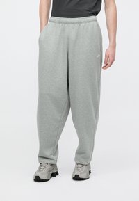 Ανοιχτό γκρι φόρμας κατασκευασμένο από μαλακό ύφασμα, με ελαστική μέση, πλαϊνές τσέπες και ένα μικρό λευκό λογότυπο στην αριστερή μηρό.