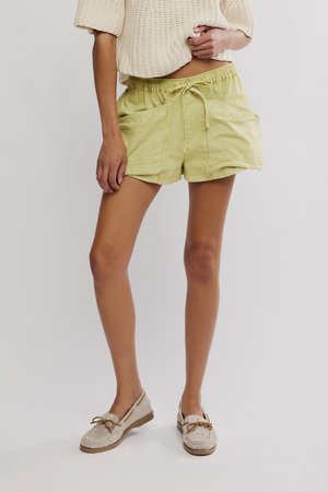 Personne portant un short à cordon de serrage vert clair avec de grandes poches avant, un pull court en tricot crème et des mocassins beige brodés.