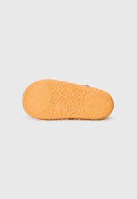 Semelle d'une sneaker avec un motif de semelle en vagues, fabriquée en caoutchouc orange, avec un détail de smiley circulaire au niveau du talon.