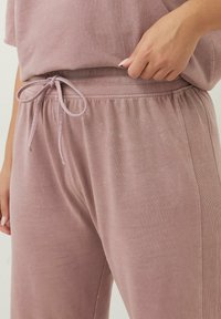 Ljust rosa loungebyxor med dragsko i midjan, tillverkade av mjukt tyg. Har en ribbad struktur och en avslappnad passform.