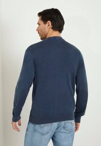 Felpa a maniche lunghe blu navy con scollatura a girocollo, polsini e orlo a coste; tessuto morbido con una texture liscia, indossata con jeans azzurri.