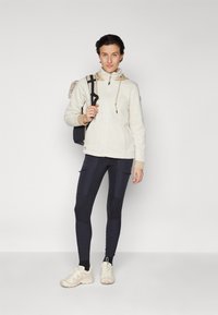 Light-colored fleece jacket with a hood, beige accents, and a zippered front, paired with dark leggings featuring textured panels and white sneakers.