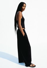 Haut sans manches noir et pantalon large noir. Tissu lisse avec une coupe décontractée. Comprend des poches latérales et des sandales noires simples.