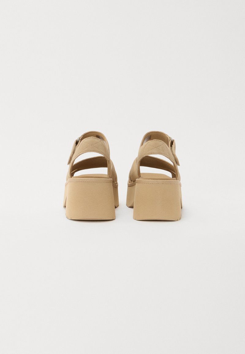 Tanfarbene Plattform-Sandalen mit offenem Rücken, breiten Riemen und einem Blockabsatz. Das Material wirkt glatt mit einer matten Oberfläche.