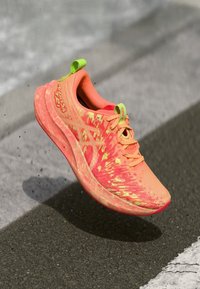 Svijetlo narančasta trkačka cipela s žutim naglascima, teksturirani gornji dio, podstavljeni ovratnik i sustav vezivanja; lagani dizajn prikladan za sportske aktivnosti.
