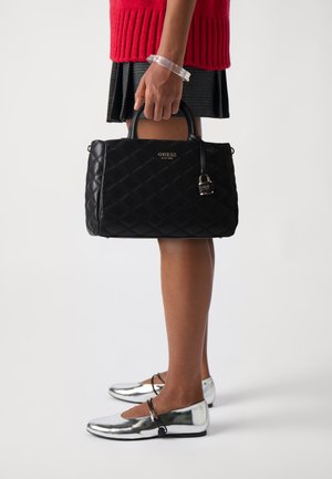 Borsa nera trapuntata con doppi manici, hardware dorato e un charm a lucchetto staccabile. Accompagnata da ballerine lucide argentate con cinturini alla caviglia.