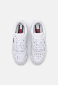 Zapatillas deportivas blancas con detalles perforados, puntera redonda y cordones planos. La marca en las plantillas presenta franjas rojas, blancas y azules.
