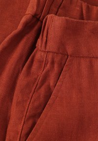 Rustfärgade linbyxor med en texturerad tygkvalitet. Funktioner inkluderar veck i midjan och sidofickor, vilket framhäver en avslappnad design.