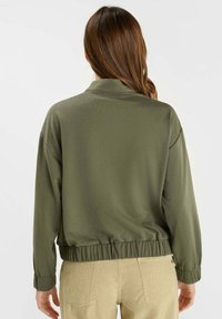 Veste légère vert olive, avec une coupe décontractée, une taille élastique et des manches longues. Design simple sans motifs ni accents visibles.