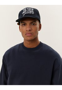 Felpa navy con scollatura tonda e logo ricamato. Abbinata a un cappellino navy con testo bianco e visiera curva.