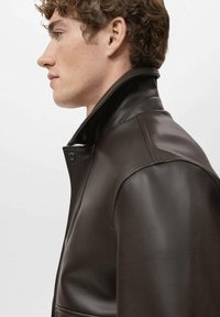 Chaqueta de cuero marrón con cuello alto y textura ligera. Cuenta con cierre de un solo botón y una silueta elegante y entallada.