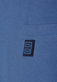 Blue fabric with a smooth texture, featuring a black label with a blue logo stitched onto a pocket. Simple, fitted design.