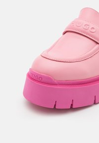 Mocassin en cuir rose avec semelle plateforme épaisse, marquage "HUGO" en relief sur la bride et le bord de la semelle, design à bout arrondi lisse.