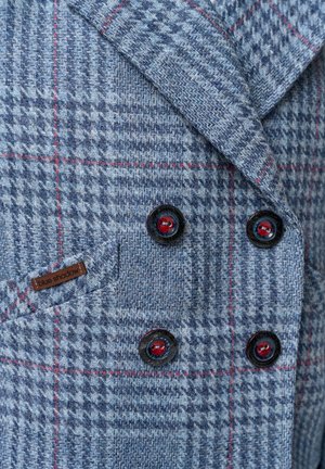 Niebieska kurtka w kratę wykonana z teksturowanej tkaniny, z czerwonym wzorem w kratę, czarnymi guzikami oraz małą metką "blue shadow".