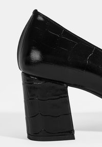 Zwarte hoge hak schoenen met een glanzende, gestructureerde bovenkant met een krokodillenpatroon en een chunky, gestructureerde blokhak.