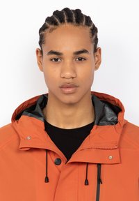 Oranje waterdichte jas met een gestructureerde zwarte voering, verstelbare trekkoorden en drukknoopdetails op de kraag.