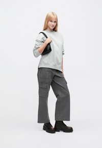 Γκρι φούτερ με ριμπ μανσέτες, συνδυασμένο με φαρδύ γκρι cargo παντελόνι με πλευρικές τσέπες. Μαύρα μποτάκια με χοντρή σόλα και κορδόνια. Μικρή μαύρη τσάντα χειρός.