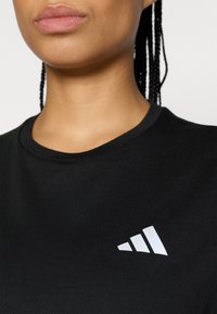 Μαύρο μπλουζάκι με κοντό μανίκι και στρογγυλή λαιμόκοψη· διαθέτει λευκό λογότυπο με τρεις γραμμές στο επάνω αριστερό μέρος του στήθους· λεία, βαμβακερή υφή.