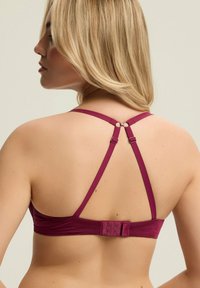 Bordowy biustonosz z cienkimi regulowanymi ramiączkami, zapięciem z tyłu i gładką teksturą. Posiada okrągłe elementy łączące ramiączka.