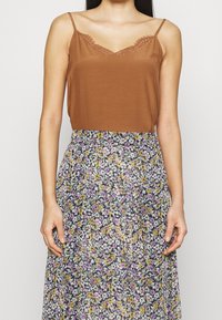 Top in raso marrone con rifiniture in pizzo abbinato a una gonna a pieghe con stampa floreale nei toni di viola, bianco e giallo.