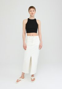 Black ribbed crop top paired with a white denim midi skirt featuring a front slit. Model wears white slide sandals. Simple design, no patterns.