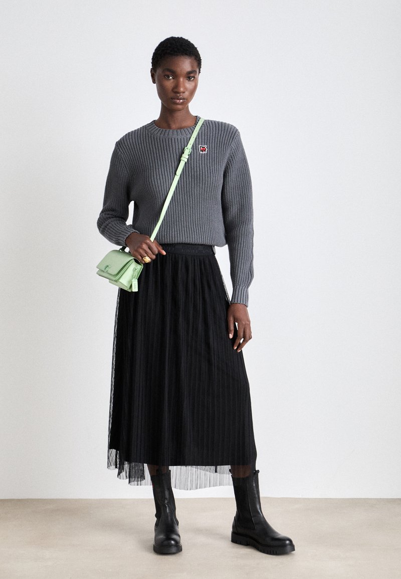 Grauer gerippter Pullover mit kleinem Logo, schwarzer Faltenrock und schwarzen Stiefeln. Hält eine mintgrüne Umhängetasche mit strukturiertem Design.