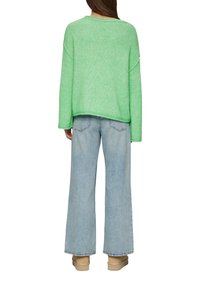 Grüner, übergroßer Strickpullover mit überschnittenen Schultern, kombiniert mit hellblauen weiten Jeans und beigen Ankle Boots, von hinten betrachtet.