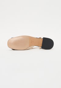 High-heeled shoe with a nude leather upper, black rubber sole, and a strap design. Texture is smooth with subtle stitching details.