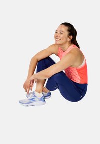 Débardeur de sport rose avec un motif géométrique, associé à un legging marin. Les chaussures présentent un design bleu et blanc avec des accents texturés.