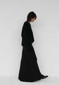 Czarny, oversize'owy sweter zestawiony z długą, lejącą się czarną spódnicą. Gładka, matowa faktura o minimalistycznym designie. Całość dopełniają czarne botki do kostki.