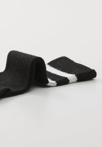 Calze nere a coste con tessuto strutturato, caratterizzate da due righe bianche orizzontali vicino alla parte superiore. La posizione arricciata mostra dettagli sul design e sul materiale.
