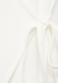 Vêtement en blanc à rayures avec une fermeture par lien. Le matériau semble doux, avec une texture lisse et des lignes épurées.