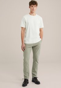 Pantaloni verzi deschisi, tricou scurt cu mâneci scurte de culoare albă crem și pantofi negri. Țesătură moale, croială ajustată și un decolteu simplu, rotund.