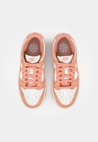 Nike sneakers featuring a pink suede upper, white leather accents, perforated toe box, and lace-up design with a flower-patterned insole.