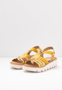 Kollane sandaal värvilise lillemustriga, elastsed ristrihmad ja paks valge tallaga, millel on laineline ääre. Sile pruun sisetald.