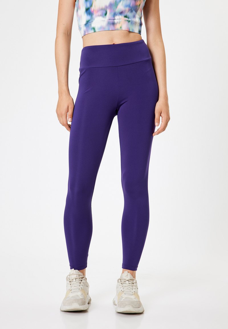 Paarse legging gemaakt van rekbaar materiaal, met een hoge taille ontwerp. Gemaakt in combinatie met een veelkleurige crop top en lichte sneakers.